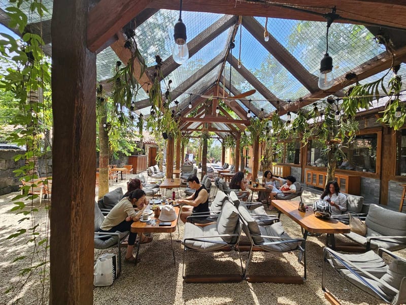 The covered dining room with a glass roof, hanging plants and cushioned seating at 7AM Bakers and 7PM Diners