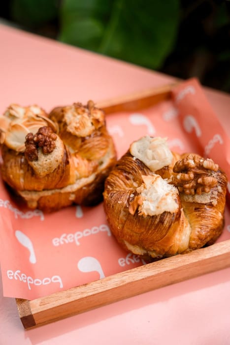 Two filled croissants in a wooden tray on pink paper at Boodaya Coffee Ubud