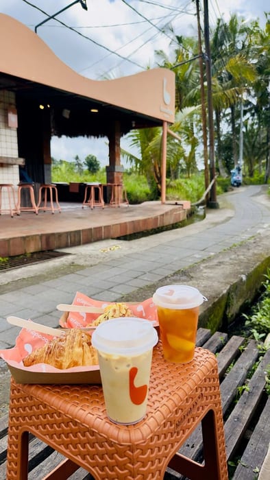 Iced drinks and a pastry on a low table on the wooden deck at Boodaya Coffee Ubud