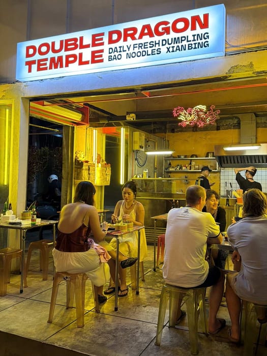 The lit Double Dragon Temple sign at night with diners inside at Double Dragon Temple