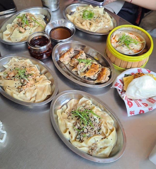 A table of dumplings, bao and sesame noodles in steel dishes at Double Dragon Temple