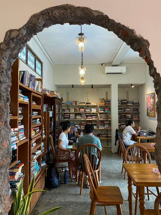 The stone archway opening onto the library room with bookshelves at Littletalks Ubud