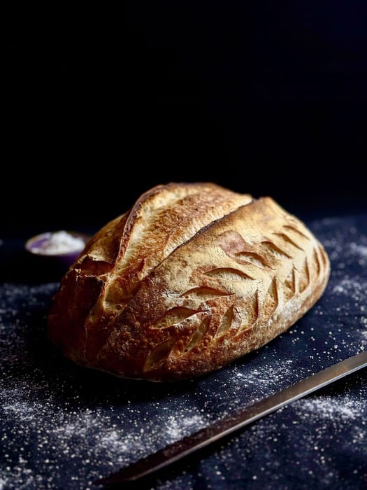A scored sourdough loaf on a floured board at Roti Bohemia