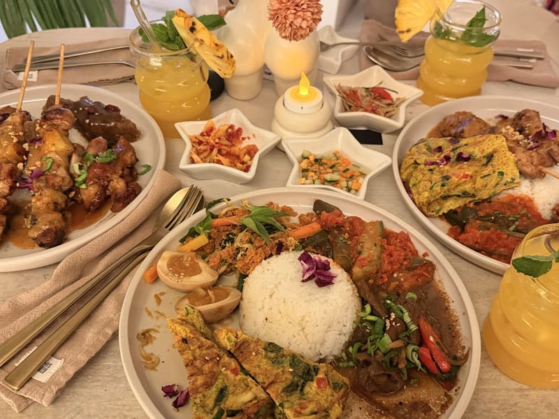A spread of satay, curries, rice bowls and juices on a table at This Is Bali