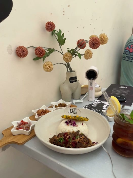 A rendang bowl with rice beside a vase of dried flowers at This Is Bali